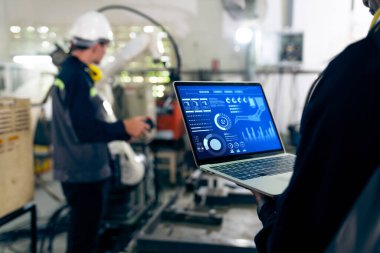 Fabrika işçileri bir atölyede usta robot kolla çalışıyorlar.