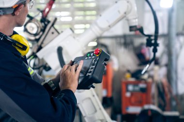 Genç fabrika işçisi usta bir robot kolla çalışıyor.