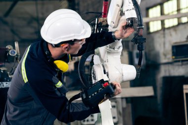 Genç fabrika işçisi usta bir robot kolla çalışıyor.