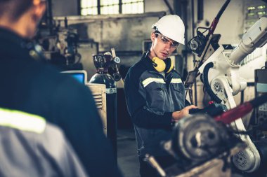 Fabrika işçileri bir atölyede usta robot kolla çalışıyorlar.