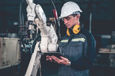 Genç fabrika işçisi usta bir robot kolla çalışıyor.