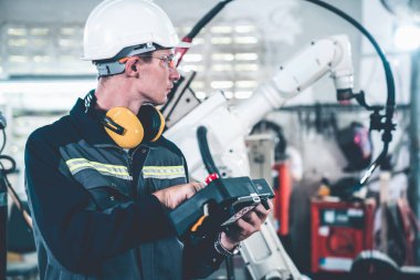 Genç fabrika işçisi usta bir robot kolla çalışıyor.