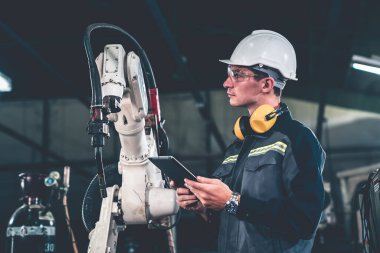 Genç fabrika işçisi usta bir robot kolla çalışıyor.