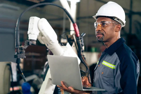 Ouvrier d'usine afro-américain travaillant avec un bras robotique compétent — Photo