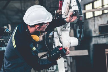 Genç fabrika işçisi usta bir robot kolla çalışıyor.