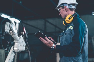 Genç fabrika işçisi usta bir robot kolla çalışıyor.