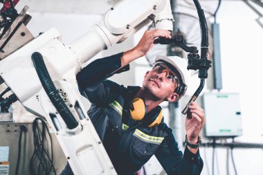 Genç fabrika işçisi usta bir robot kolla çalışıyor.