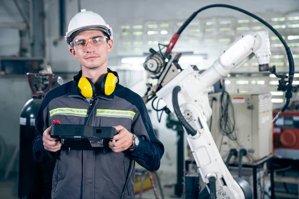 Jeune ouvrier d'usine travaillant avec un bras robotique compétent — Photo