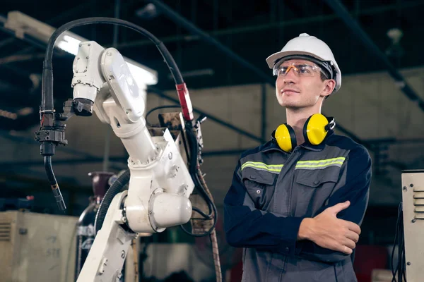 Молодий заводський працівник, що працює з майстерною роботизованою рукою — стокове фото
