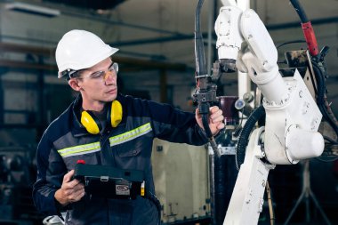 Genç fabrika işçisi usta bir robot kolla çalışıyor.