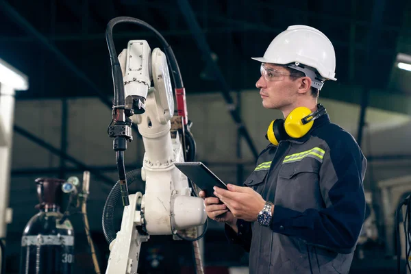 Jeune ouvrier d'usine travaillant avec un bras robotique compétent — Photo