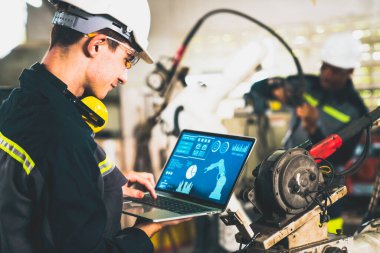 Genç fabrika işçisi usta bir robot kolla çalışıyor.