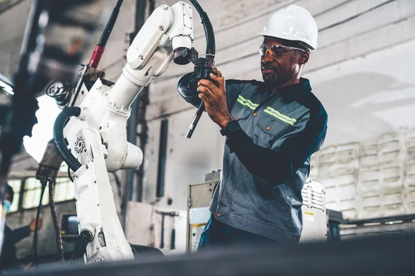 Ouvrier d'usine afro-américain travaillant avec un bras robotique compétent — Photo