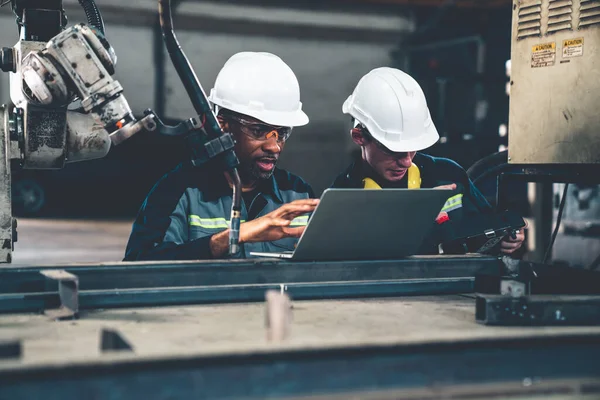 Fabrika işçileri bir atölyede usta robot kolla çalışıyorlar.