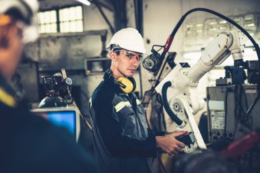 Fabrika işçileri bir atölyede usta robot kolla çalışıyorlar.