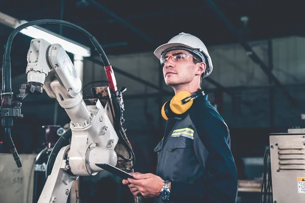 Genç fabrika işçisi usta bir robot kolla çalışıyor.