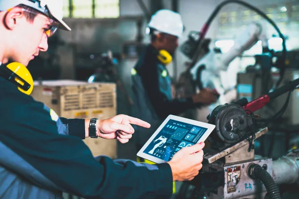 Fabrika işçileri bir atölyede usta robot kolla çalışıyorlar.