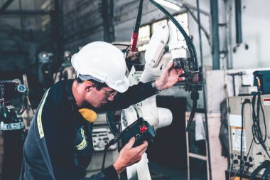 Genç fabrika işçisi usta bir robot kolla çalışıyor.