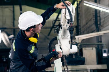 Genç fabrika işçisi usta bir robot kolla çalışıyor.