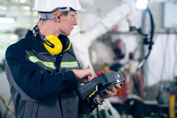 Jeune ouvrier d'usine travaillant avec un bras robotique compétent — Photo