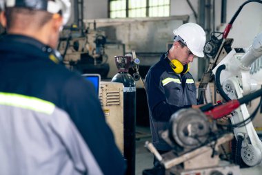 Fabrika işçileri bir atölyede usta robot kolla çalışıyorlar.
