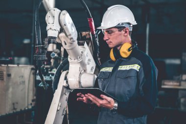 Genç fabrika işçisi usta bir robot kolla çalışıyor.