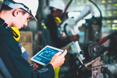 Fabrika işçileri bir atölyede usta robot kolla çalışıyorlar.