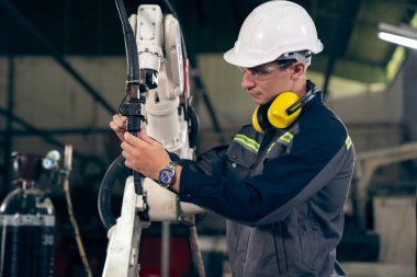 Bir atölyede usta bir robot kolla çalışan genç bir fabrika işçisi. Otomatik üretim teknolojisi için endüstriyel robot programlama yazılımı .