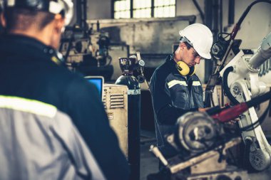 Fabrika işçileri bir atölyede uzman robot kolla çalışıyorlar. Otomatik üretim teknolojisi için endüstriyel robot programlama yazılımı .