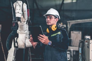 Bir atölyede usta bir robot kolla çalışan genç bir fabrika işçisi. Otomatik üretim teknolojisi için endüstriyel robot programlama yazılımı .