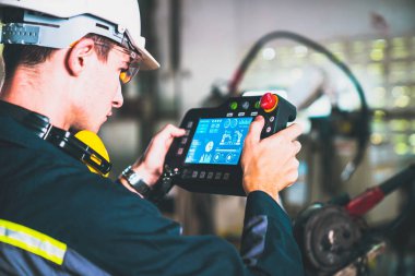 Bir atölyede usta bir robot kolla çalışan genç bir fabrika işçisi. Otomatik üretim teknolojisi için endüstriyel robot programlama yazılımı .