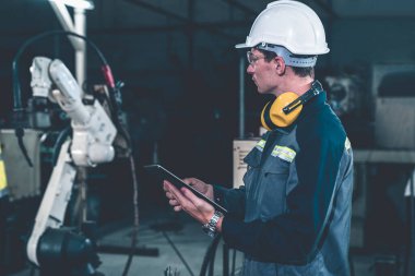 Bir atölyede usta bir robot kolla çalışan genç bir fabrika işçisi. Otomatik üretim teknolojisi için endüstriyel robot programlama yazılımı .