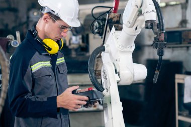 Bir atölyede usta bir robot kolla çalışan genç bir fabrika işçisi. Otomatik üretim teknolojisi için endüstriyel robot programlama yazılımı .