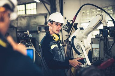 Fabrika işçileri bir atölyede uzman robot kolla çalışıyorlar. Otomatik üretim teknolojisi için endüstriyel robot programlama yazılımı .