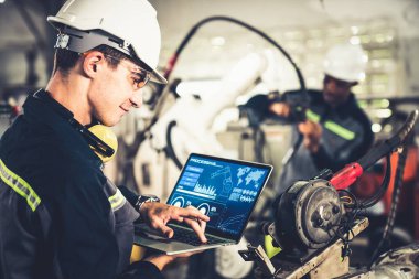 Bir atölyede usta bir robot kolla çalışan genç bir fabrika işçisi. Otomatik üretim teknolojisi için endüstriyel robot programlama yazılımı .