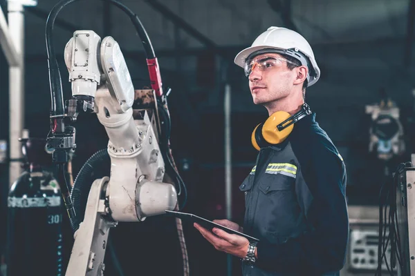 Young factory worker working with adept robotic arm in a workshop . Industry robot programming software for automated manufacturing technology .