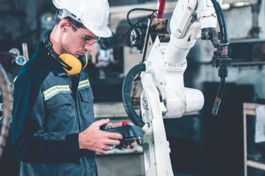 Bir atölyede usta bir robot kolla çalışan genç bir fabrika işçisi. Otomatik üretim teknolojisi için endüstriyel robot programlama yazılımı .