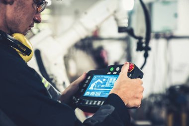 Bir atölyede usta bir robot kolla çalışan genç bir fabrika işçisi. Otomatik üretim teknolojisi için endüstriyel robot programlama yazılımı .