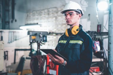 Bir atölye binasında usta tablet bilgisayar kullanan genç bir fabrika işçisi. Endüstriyel teknoloji ve imalat yazılım yapılandırması .