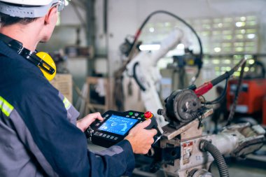 Bir atölyede usta bir robot kolla çalışan genç bir fabrika işçisi. Otomatik üretim teknolojisi için endüstriyel robot programlama yazılımı .