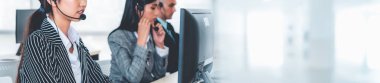 Geniş görünüm panorama panorama pankartındaki çağrı merkezi ya da müşteri destek ajansı, telefon konferansında uzak müşteri ya da iş arkadaşını desteklemek için ofiste çalışırken kulaklık takıyor.