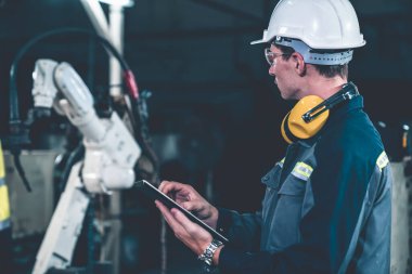 Bir atölyede usta bir robot kolla çalışan genç bir fabrika işçisi. Otomatik üretim teknolojisi için endüstriyel robot programlama yazılımı .