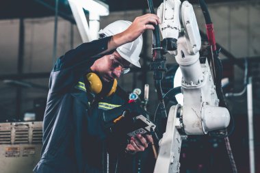 Bir atölyede usta bir robot kolla çalışan genç bir fabrika işçisi. Otomatik üretim teknolojisi için endüstriyel robot programlama yazılımı .