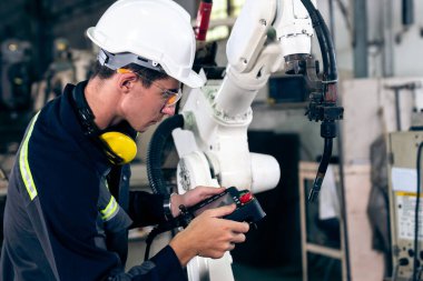 Bir atölyede usta bir robot kolla çalışan genç bir fabrika işçisi. Otomatik üretim teknolojisi için endüstriyel robot programlama yazılımı .