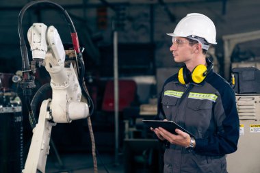 Bir atölyede usta bir robot kolla çalışan genç bir fabrika işçisi. Otomatik üretim teknolojisi için endüstriyel robot programlama yazılımı .