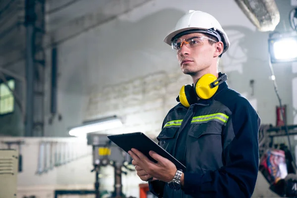 Young factory worker using adept tablet computer in a workshop building . Industrial technology and manufacturing software configuration .