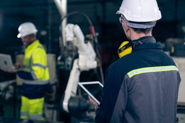 Fabrika işçileri bir atölyede uzman robot kolla çalışıyorlar. Otomatik üretim teknolojisi için endüstriyel robot programlama yazılımı .