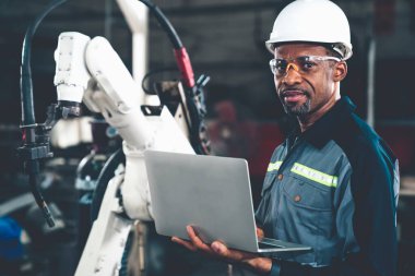 Afrika kökenli Amerikalı bir fabrika işçisi bir atölyede uzman bir robot kolla çalışıyor. Otomatik üretim teknolojisi için endüstriyel robot programlama yazılımı .