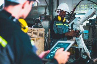 Fabrika işçileri bir atölyede uzman robot kolla çalışıyorlar. Otomatik üretim teknolojisi için endüstriyel robot programlama yazılımı .