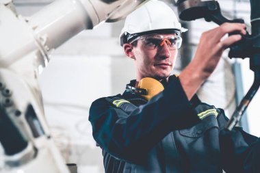 Bir atölyede usta bir robot kolla çalışan genç bir fabrika işçisi. Otomatik üretim teknolojisi için endüstriyel robot programlama yazılımı .